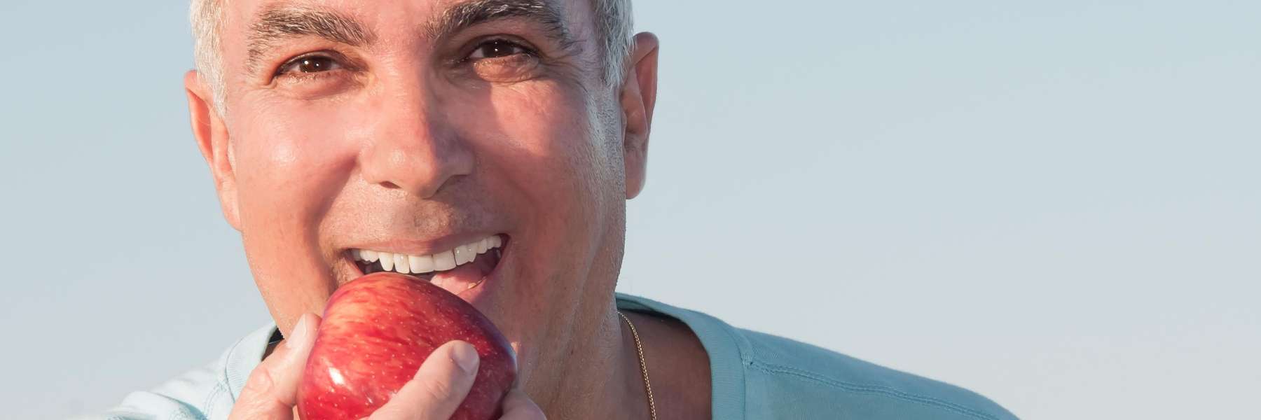 An image of a man holding an apple in his hand and taking a bite